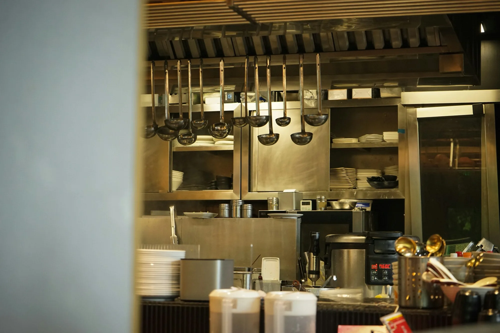 A hip open restaurant kitchen with hanging ladles, organized stainless steel prep stations, and digital timers — the modern operation where automation lives alongside human craft